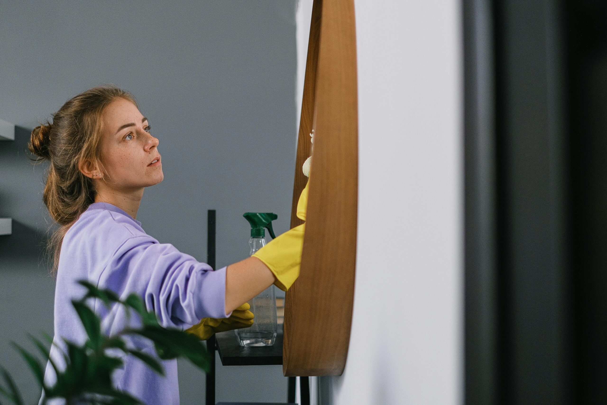 woman in a purple jumper with yellow gloves cleaning a mirror<br />
